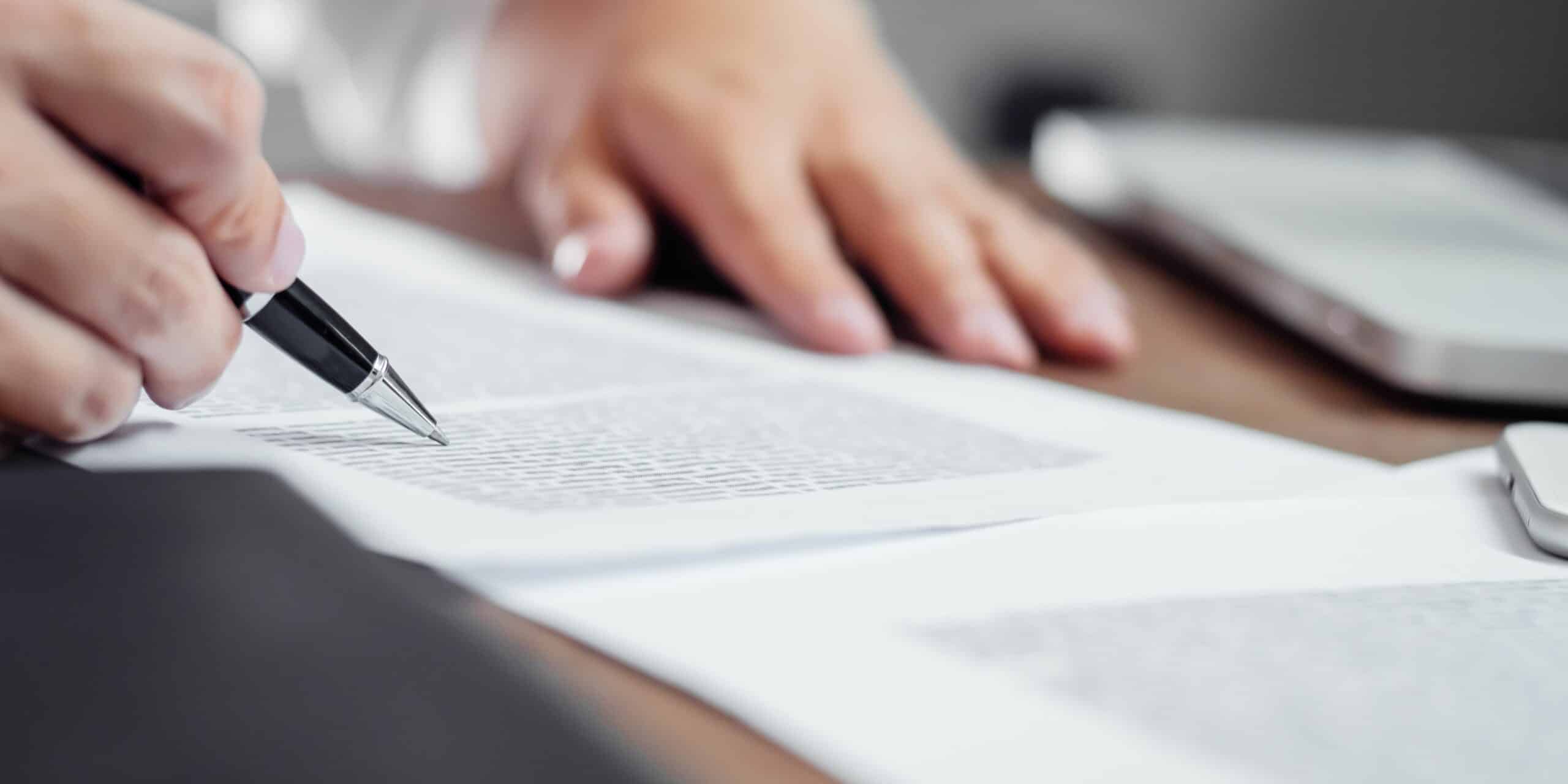 Picture of a hand holding a pen going through a document.
